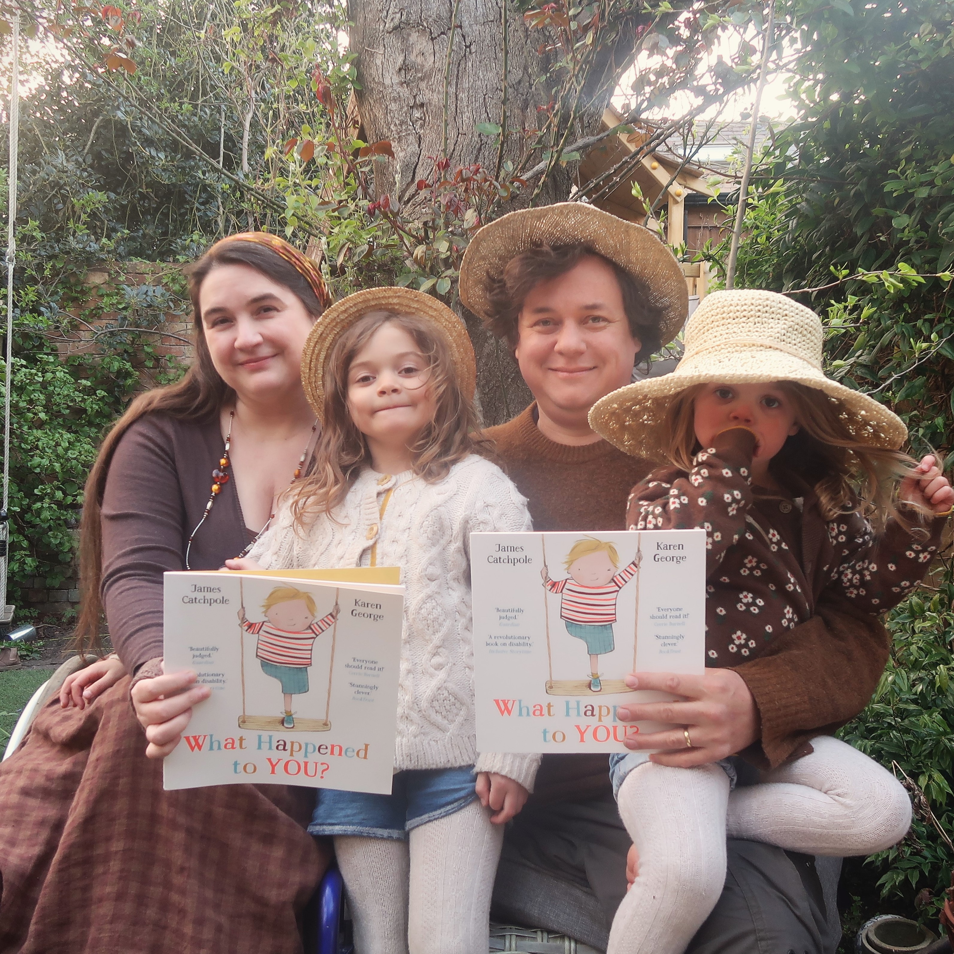 James and Lucy Catchpole and their children holding a copy of the What Happened to You picture book. They're a disabled couple with brown hair.