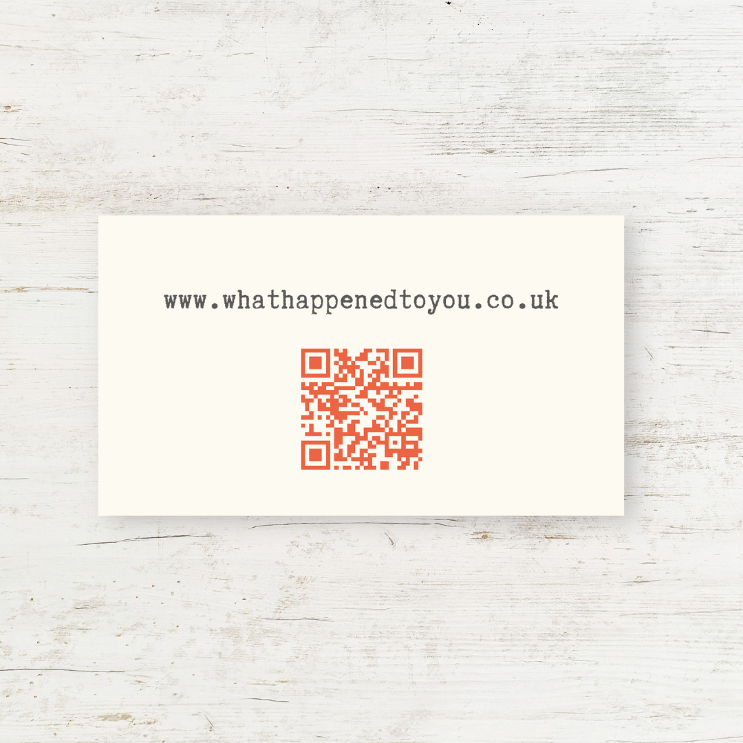 A small cream business-sized card with a muted red QR code and the url www.whathappenedtoyou.co.uk - on a white wood background.